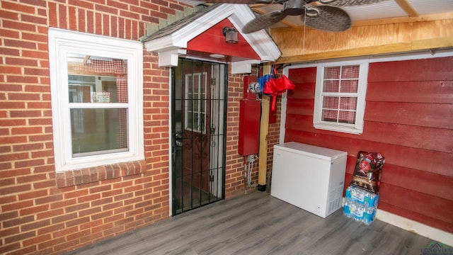 view of exterior entry with ceiling fan and brick siding