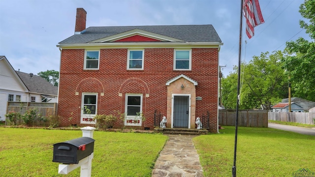 colonial home featuring brick siding, fence, and a front yard