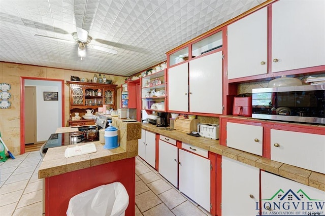 kitchen featuring a center island, light tile patterned floors, white cabinets, ceiling fan, and stove