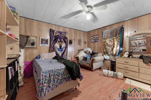 bedroom featuring wooden walls, ceiling fan, and light hardwood / wood-style flooring