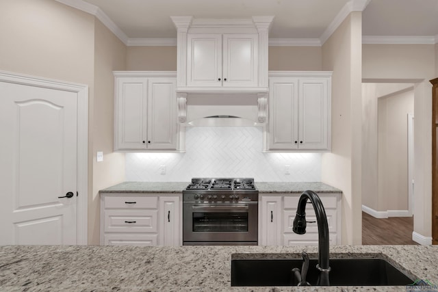 kitchen featuring sink, high end stainless steel range oven, ornamental molding, light stone counters, and white cabinetry