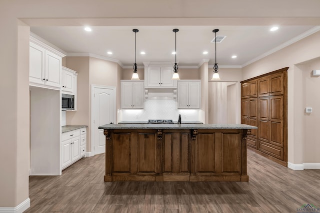 kitchen with decorative light fixtures, white cabinetry, an island with sink, and premium range hood