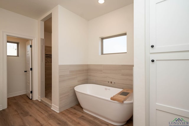 bathroom featuring hardwood / wood-style floors, a tub to relax in, and tile walls