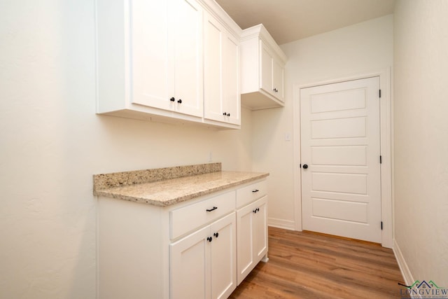 kitchen with light hardwood / wood-style floors, white cabinetry, and light stone counters