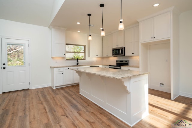 kitchen featuring appliances with stainless steel finishes, a center island, white cabinetry, sink, and hanging light fixtures