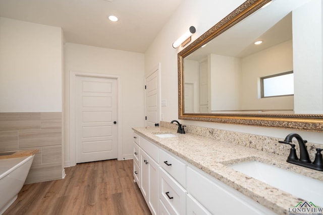 bathroom with vanity, a bath, tile walls, and wood-type flooring