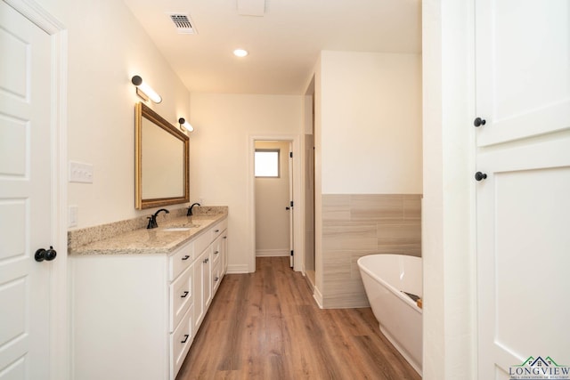 bathroom with vanity, hardwood / wood-style flooring, a tub, and tile walls