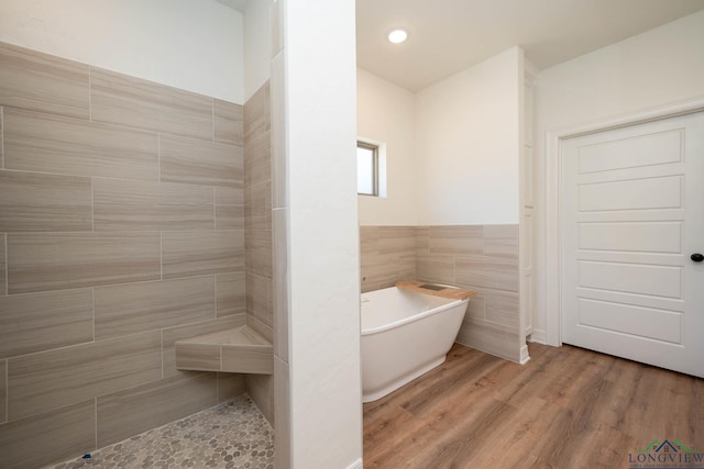 bathroom with a tub, wood-type flooring, and tile walls