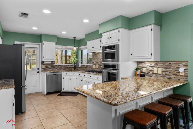 327 Forest Hls, Hallsville, TX 75650 - kitchen featuring appliances with stainless steel finishes, a peninsula, light stone countertops, tasteful backsplash, and white cabinets