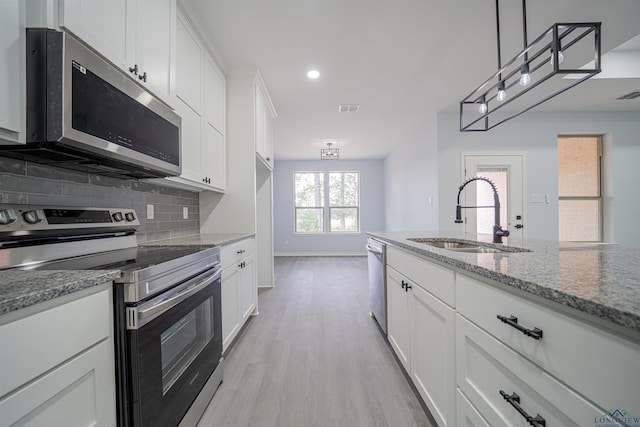 kitchen with pendant lighting, sink, appliances with stainless steel finishes, light stone counters, and white cabinetry