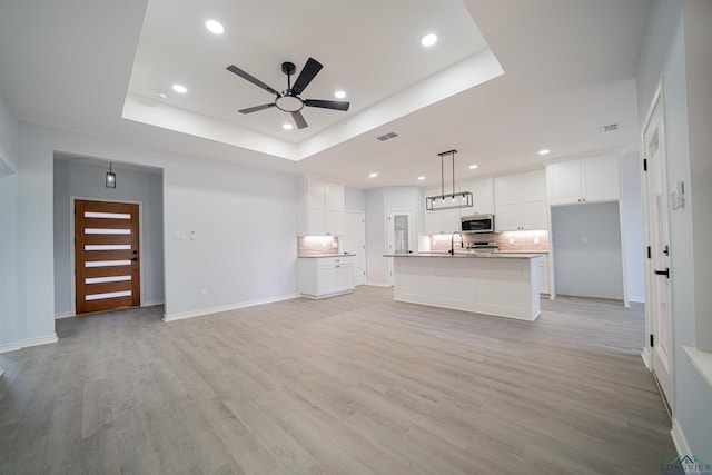 unfurnished living room with a tray ceiling, ceiling fan, sink, and light wood-type flooring