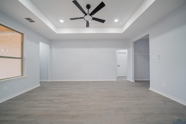 unfurnished room with a raised ceiling, ceiling fan, and light hardwood / wood-style floors