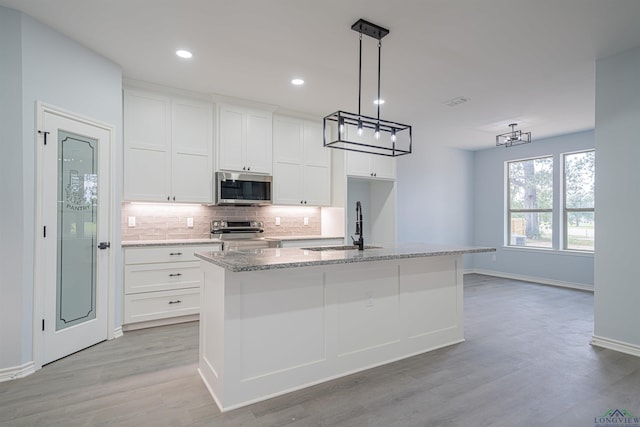 kitchen with appliances with stainless steel finishes, a kitchen island with sink, sink, decorative light fixtures, and white cabinetry