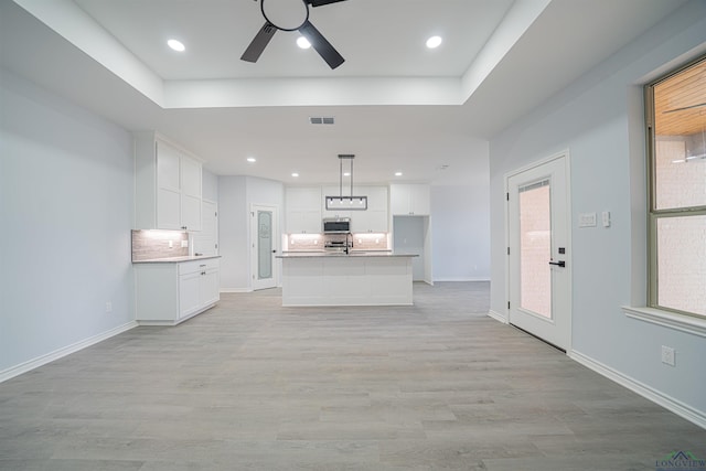 unfurnished living room with a raised ceiling, ceiling fan, a healthy amount of sunlight, and light wood-type flooring