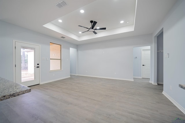 interior space with ceiling fan, a raised ceiling, and light hardwood / wood-style flooring