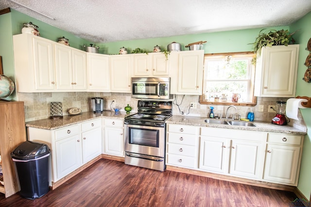 kitchen featuring appliances with stainless steel finishes, a textured ceiling, dark wood-type flooring, and a sink