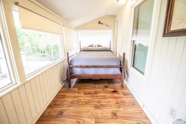bedroom featuring light wood finished floors, wood walls, and vaulted ceiling