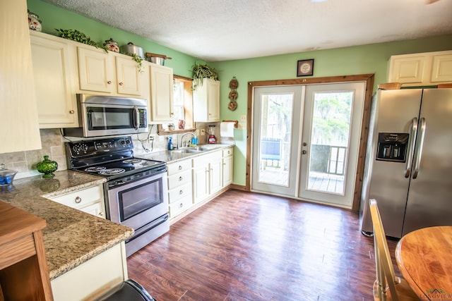 kitchen with light stone counters, a sink, french doors, stainless steel appliances, and wood finished floors