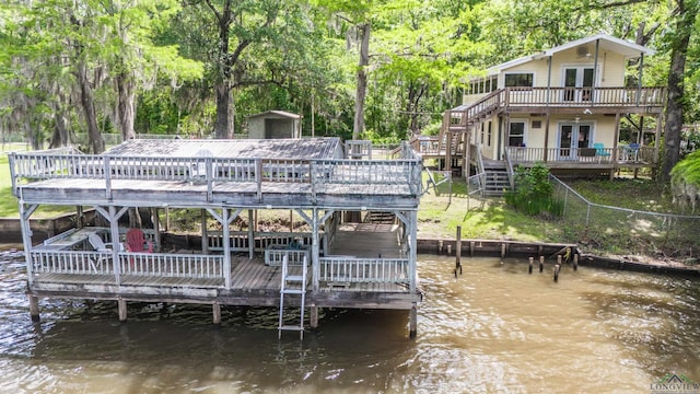 rear view of house with an outbuilding, a storage shed, stairway, a deck with water view, and french doors