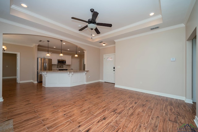 unfurnished living room with hardwood / wood-style flooring, ceiling fan, a tray ceiling, and crown molding