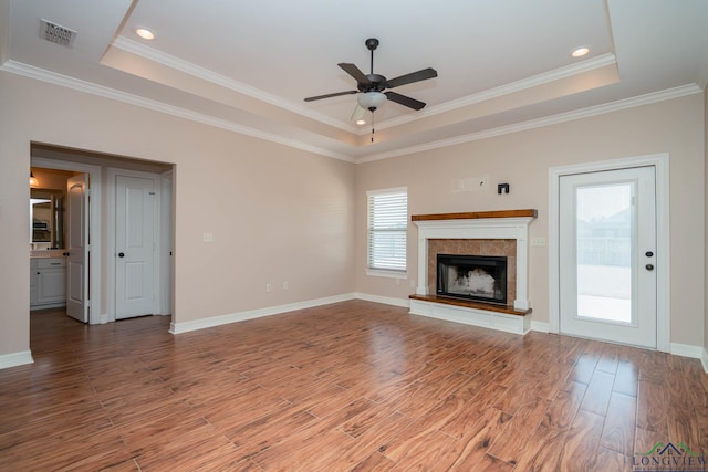 unfurnished living room with a tile fireplace, ceiling fan, wood-type flooring, ornamental molding, and a raised ceiling