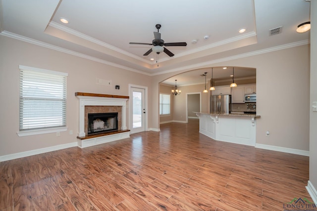 unfurnished living room with a raised ceiling, ceiling fan with notable chandelier, and light hardwood / wood-style flooring