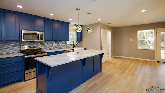 kitchen with a kitchen breakfast bar, blue cabinetry, appliances with stainless steel finishes, a kitchen island, and light stone counters