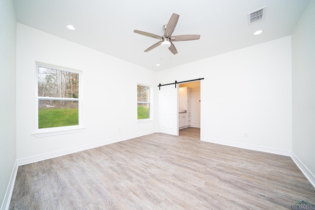 unfurnished bedroom featuring ceiling fan, a barn door, light hardwood / wood-style floors, and multiple windows