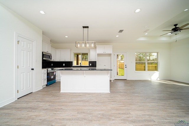 kitchen with pendant lighting, a center island, a raised ceiling, appliances with stainless steel finishes, and white cabinetry