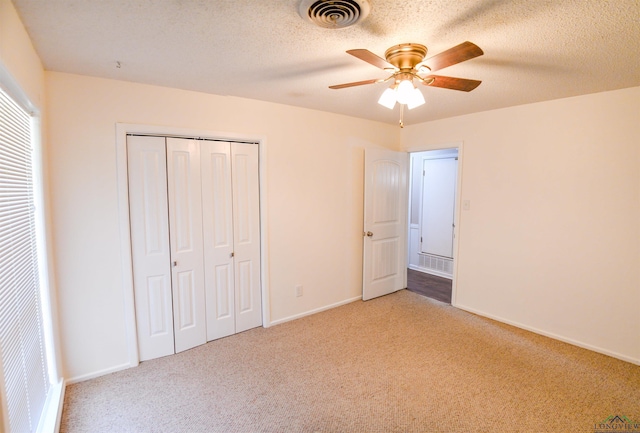 unfurnished bedroom featuring light colored carpet, a textured ceiling, ceiling fan, and a closet