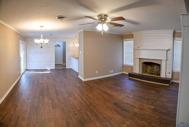 unfurnished living room featuring ceiling fan with notable chandelier, wood walls, dark hardwood / wood-style flooring, ornamental molding, and a brick fireplace