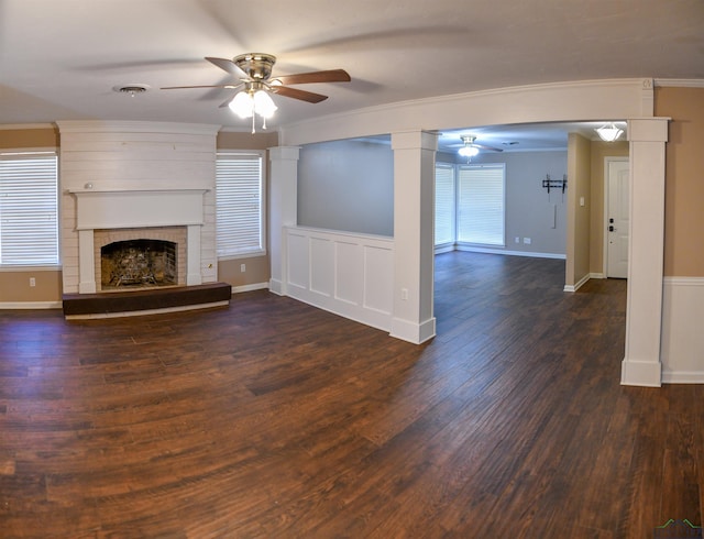 unfurnished living room featuring ornamental molding, a brick fireplace, dark wood-type flooring, and ceiling fan