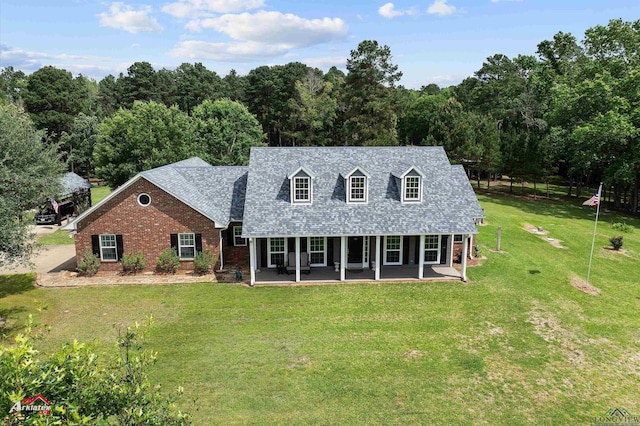 rear view of property featuring roof with shingles, brick siding, a forest view, a patio, and a yard