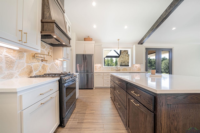 kitchen featuring black range with gas stovetop, beam ceiling, white cabinets, stainless steel refrigerator, and hanging light fixtures