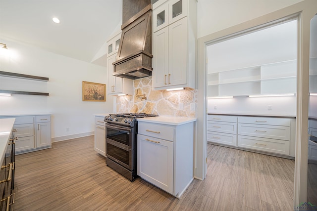 kitchen with custom exhaust hood, light hardwood / wood-style flooring, white cabinets, lofted ceiling, and stainless steel range with gas stovetop