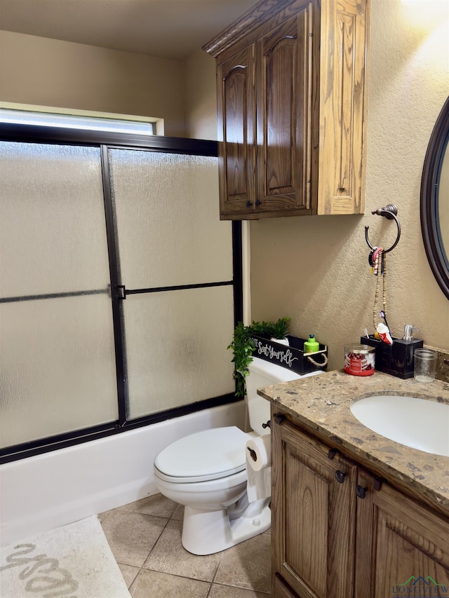 full bathroom featuring toilet, a textured wall, tile patterned floors, shower / bath combination with glass door, and vanity