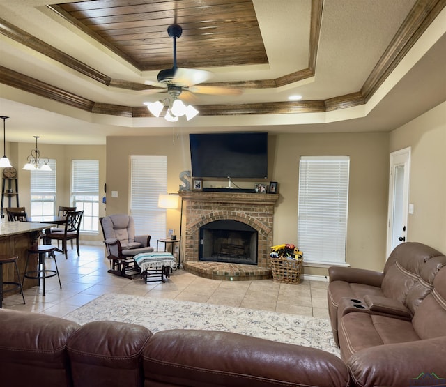 living room featuring crown molding, a tray ceiling, light tile patterned floors, a fireplace, and a ceiling fan