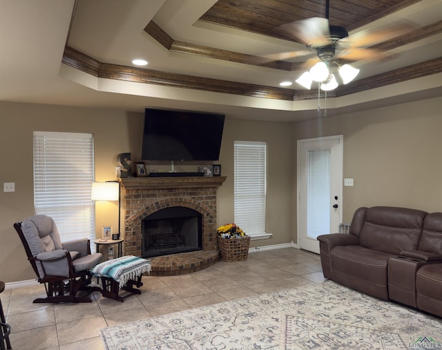 living area featuring a raised ceiling, crown molding, tile patterned flooring, baseboards, and a brick fireplace