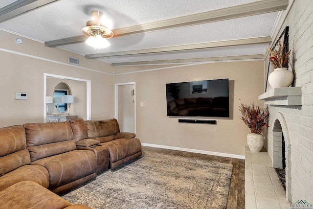 living room with ceiling fan, beamed ceiling, a textured ceiling, a fireplace, and hardwood / wood-style flooring