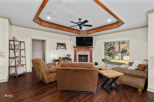 living room featuring a raised ceiling, ceiling fan, ornamental molding, and a brick fireplace