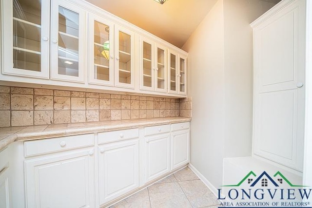 bar featuring decorative backsplash, white cabinetry, light tile patterned floors, and vaulted ceiling