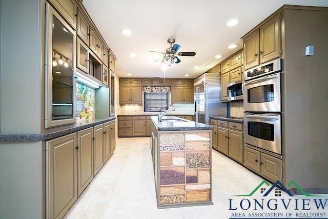 kitchen with a kitchen island with sink, sink, ceiling fan, tasteful backsplash, and stainless steel appliances