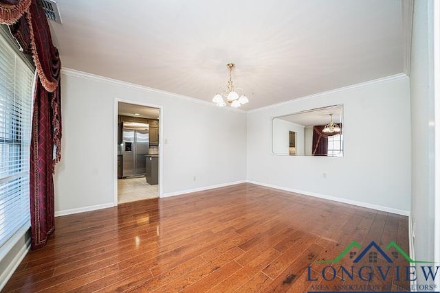 empty room featuring a healthy amount of sunlight, crown molding, wood-type flooring, and a notable chandelier