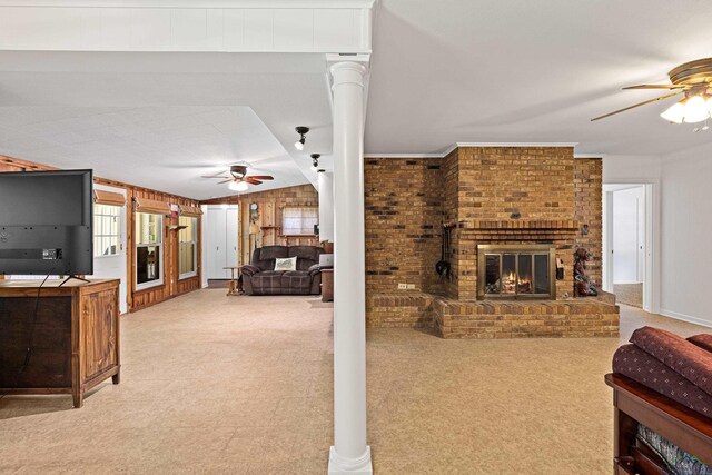 living room featuring decorative columns, ornamental molding, ceiling fan, a fireplace, and wood walls