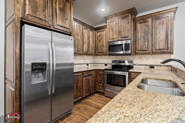 kitchen with appliances with stainless steel finishes, backsplash, light stone counters, sink, and dark hardwood / wood-style floors