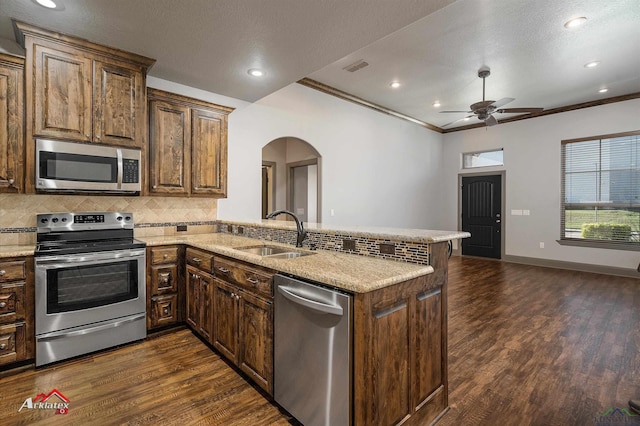 kitchen with sink, ornamental molding, dark hardwood / wood-style flooring, kitchen peninsula, and stainless steel appliances