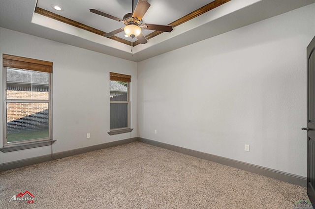 empty room with carpet flooring, ceiling fan, ornamental molding, and a tray ceiling