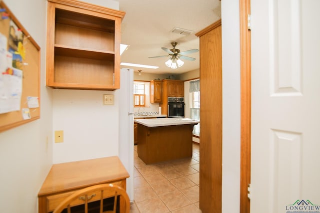 kitchen with a breakfast bar, a center island, ceiling fan, black oven, and light tile patterned flooring