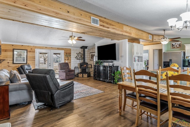 dining area featuring dark wood-type flooring, ceiling fan with notable chandelier, wooden walls, and a wood stove