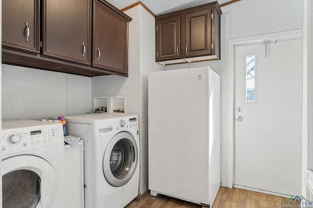 clothes washing area featuring cabinets, hardwood / wood-style floors, and washing machine and clothes dryer